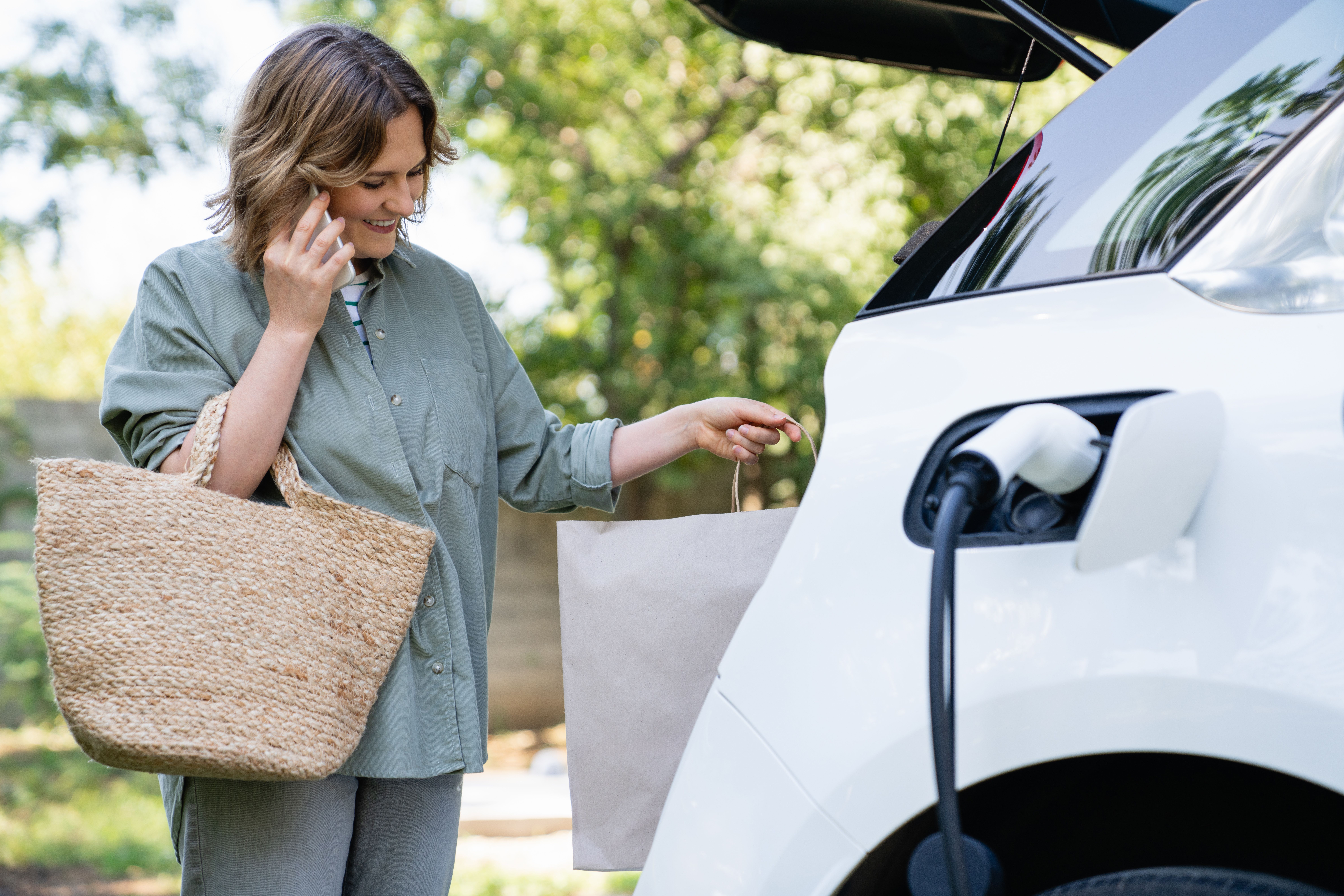 Solaranlage: Frau mit Einkaufstaschen neben E-Auto beim Laden