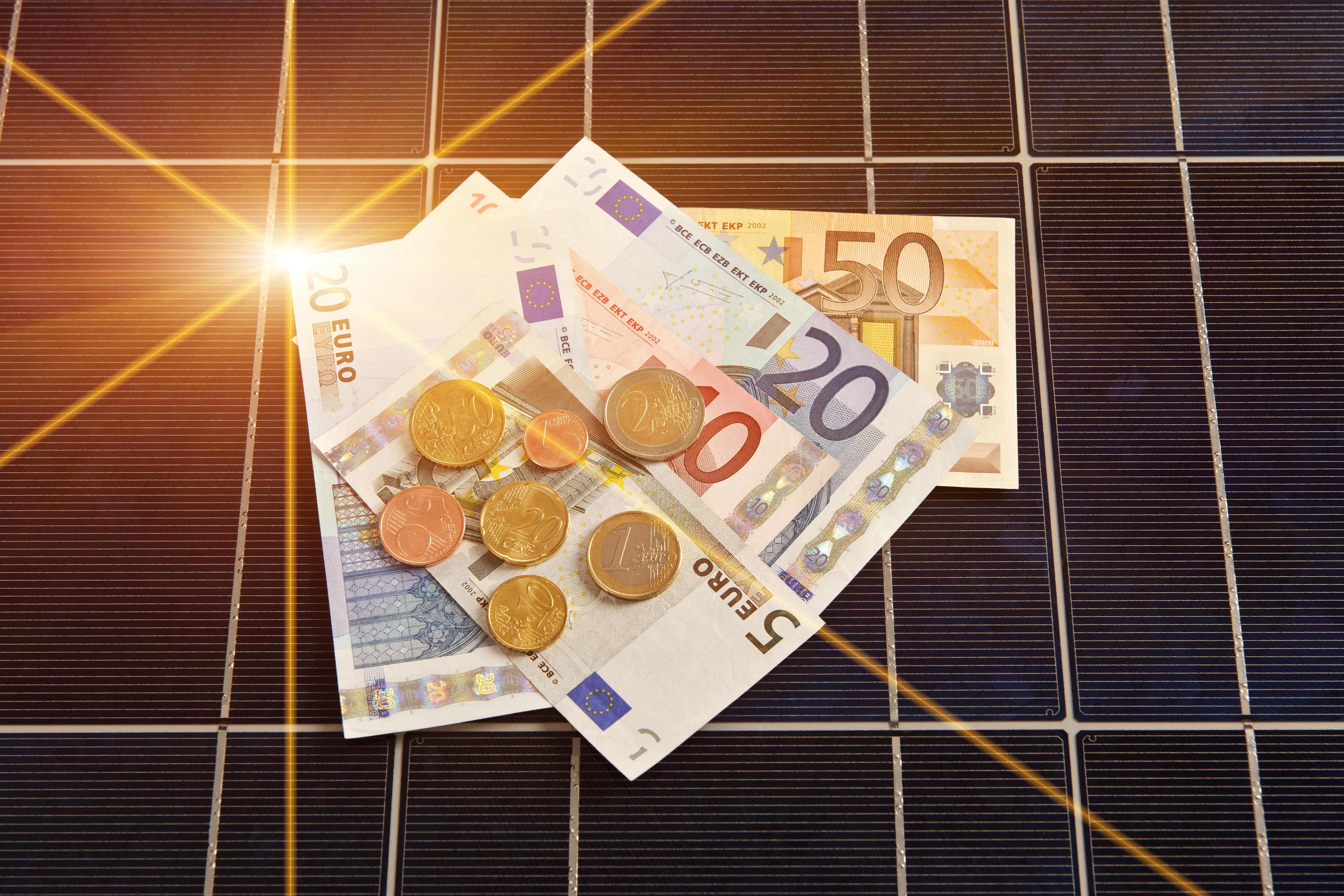 Geldscheine und Münzen auf einem schwarzen, sonnenbeschienenen Solarmodule